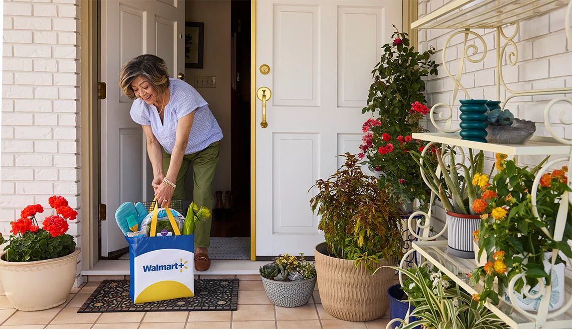 Woman collecting her Walmart Plus delivery bag off the porch of her home with potted plants decorating the patio